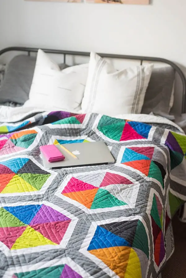 Bed with bright colorful quilt and laptop on top of bed.